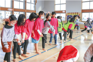 子どもたちが一直線に並び、スポンジでできた小さなプレゼントの箱を投げている写真