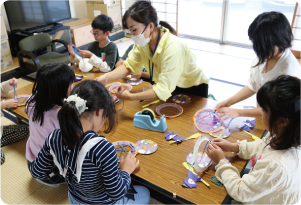 テーブルで児童館職員と子どもたちが一緒に作業をしている写真